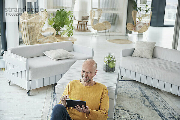 Älterer Mann  der ein digitales Tablet benutzt  während er zu Hause auf dem Boden sitzt