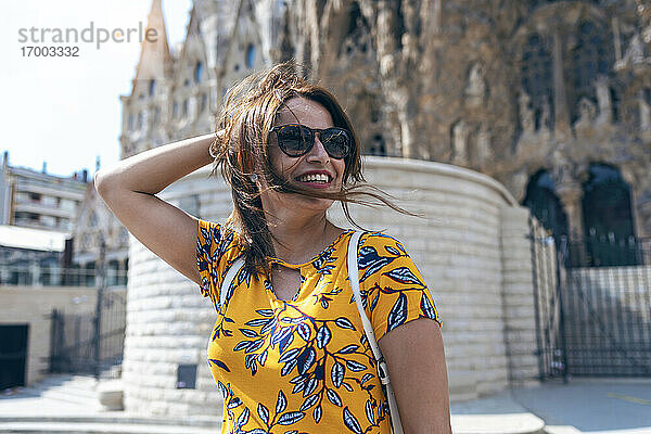 Mittlere erwachsene Frau  die lächelnd vor der Sagrada Familia in Barcelona  Katalonien  Spanien steht