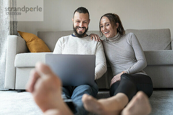Paar lacht  während es im Wohnzimmer einen Film auf dem Laptop ansieht
