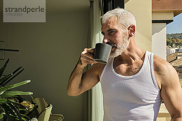 Älterer Mann trinkt Morgenkaffee im Wohnzimmer an einem sonnigen Tag