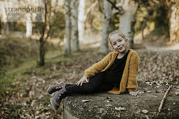 Lächelndes Mädchen entspannt sich auf einer Betonbank im Wald im Herbst