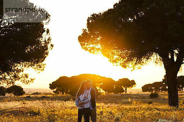 Romantisches junges Paar steht auf einem landwirtschaftlichen Feld bei Sonnenuntergang