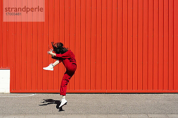 Frau in rotem Overall springt vor rotem Rolltor in die Luft