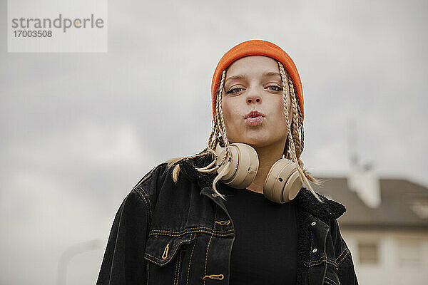 Hipster-Frau mit Kopfhörern und Strickmütze  die ein Gesicht gegen den Himmel macht