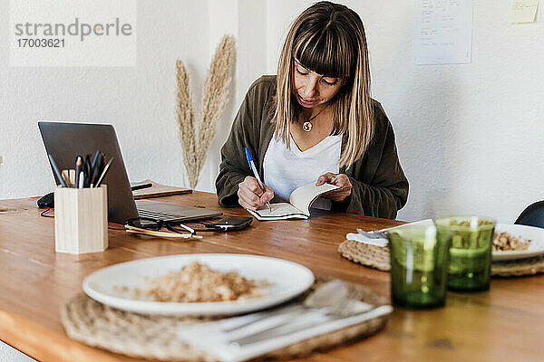 Weibliche Fachkraft mit Speiseteller auf dem Tisch  die auf einem Notizblock im Heimbüro schreibt