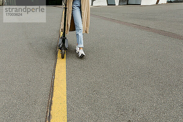 Frau zu Fuß mit Elektro-Scooter auf Straßenmarkierung