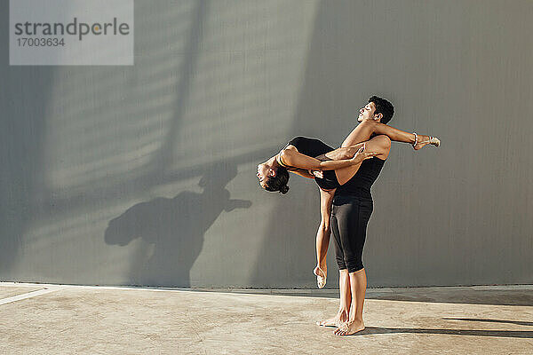 Junger Mann hilft flexible Frau tun Tanz Pose gegen die Wand