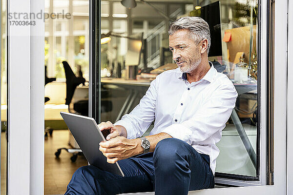 Geschäftsmann  der im Büro sitzend an einem digitalen Tablet arbeitet