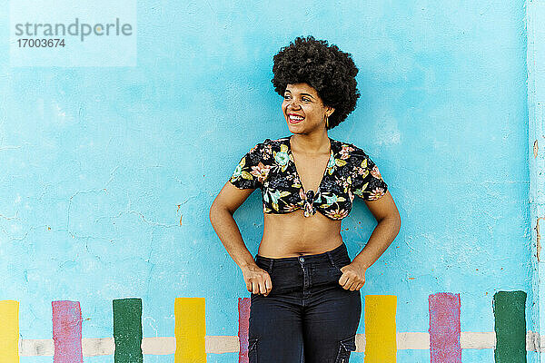 Lächelnde afroamerikanische Frau vor einer blauen Wand mit Blick zur Seite