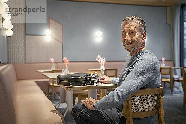 Lächelnder Geschäftsmann mit Aktentasche in einem modernen Café