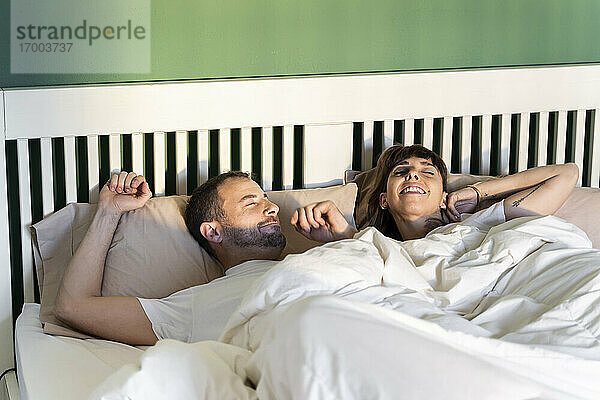 Lächelndes Paar  das langsam aufwacht  während es zu Hause im Bett liegt