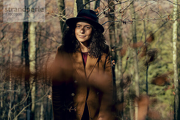 Ältere Frau mit Hut und Jacke im Wald stehend