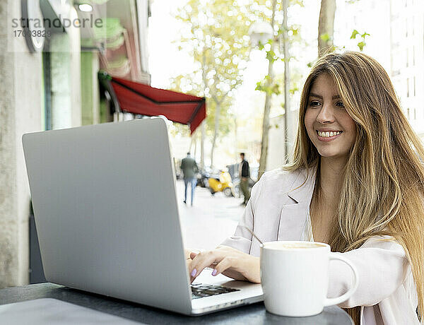 Junge Frau lächelt bei der Arbeit am Laptop im Café