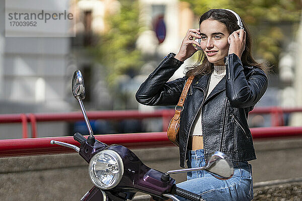 Lächelnde Frau mit Kopfhörern auf einem Motorroller