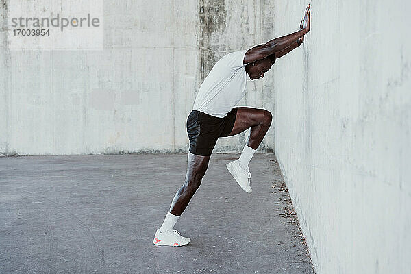 Sportler beim Stretching-Training  während er sich an eine weiße Wand lehnt