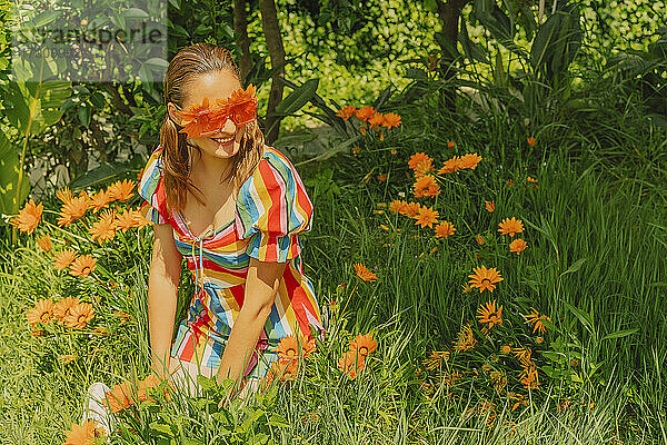 Porträt einer glücklichen Frau in der Natur  die eine Brille mit orangefarbenen Blumen trägt  die ihre Augen bedecken
