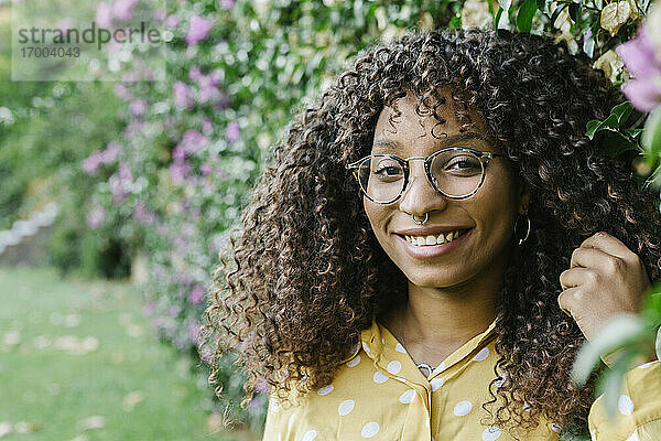Lächelnde Frau mit Brille an einer grünen Pflanzenwand im Park