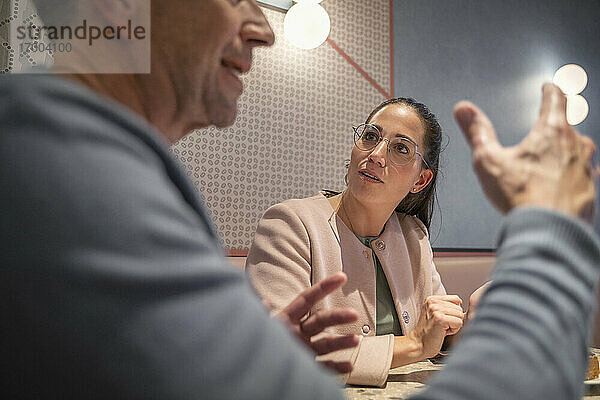 Geschäftsfrau hört einem Kollegen zu  während sie in einem modernen Cafe sitzt