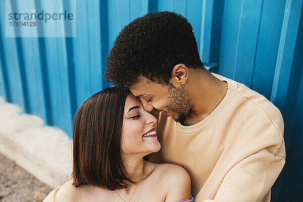 Lächelndes junges Paar sitzt von Angesicht zu Angesicht an einer blauen Wand