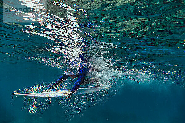 Männlicher Surfer taucht mit Surfbrett im Meer auf den Malediven