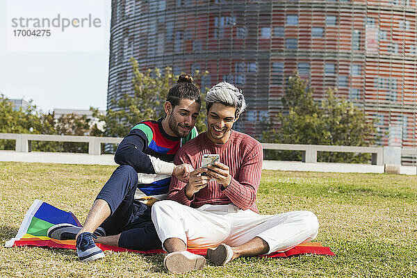 Lächelnder Mann mit schwulem Partner  der im Park ein Mobiltelefon benutzt