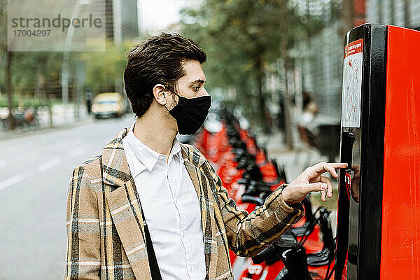 Junger Mann mit Gesichtsmaske mietet Fahrrad in der Stadt