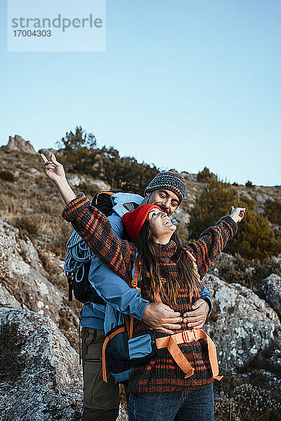Glücklicher Freund umarmt Freundin stehend mit ausgestreckten Armen auf Berg im Urlaub