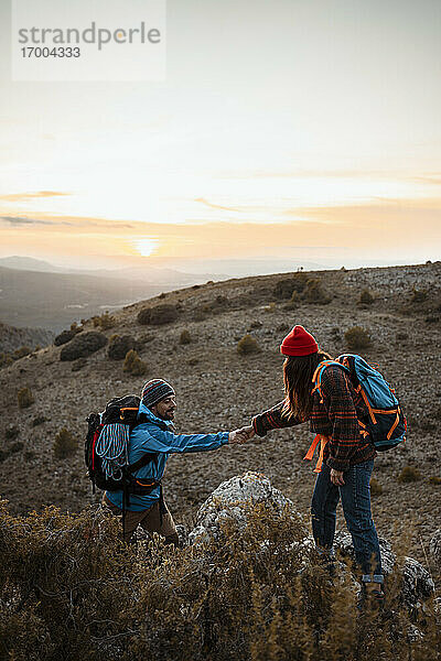 Freundin hält Hand von Freund Klettern felsigen Berg gegen den Himmel bei Sonnenuntergang