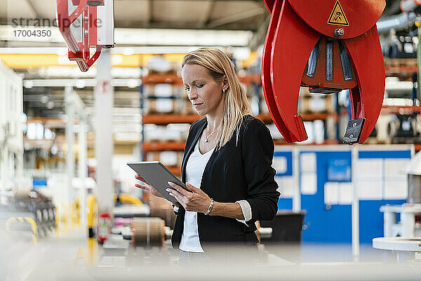 Blonde Geschäftsfrau  die ein digitales Tablet benutzt  während sie in einer Fabrik steht