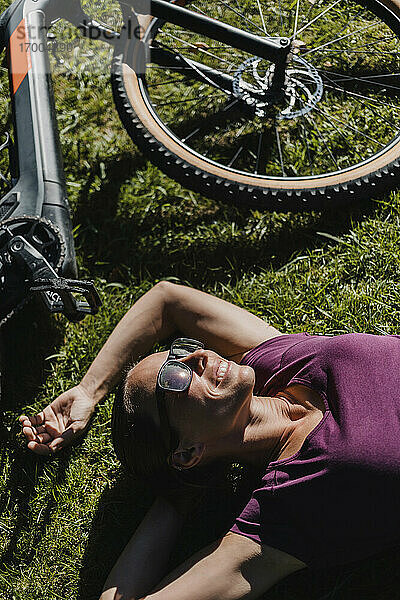 Lächelnde Frau ruht sich aus  während sie mit ihrem Mountainbike im Park im Gras liegt