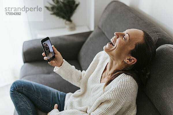 Frau lacht während eines Videogesprächs mit einem männlichen Freund im heimischen Wohnzimmer