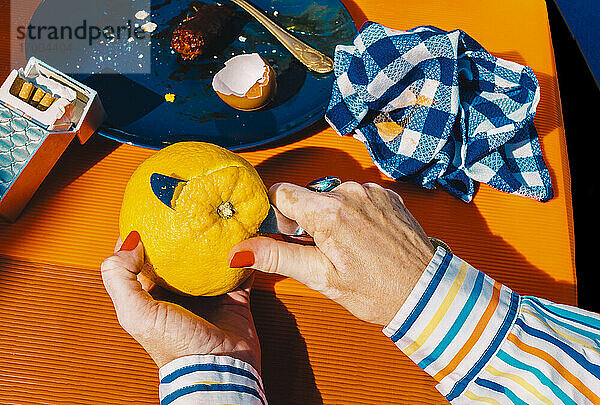 Hände einer älteren Frau  die eine Orange mit einem Tafelmesser schält