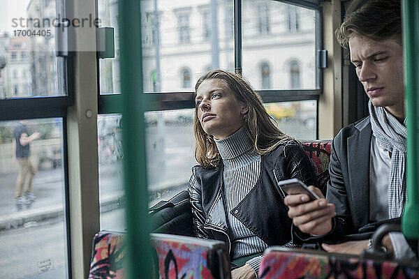 Nachdenkliche Frau  die mit einem männlichen Kollegen im Bus sitzt und ein Smartphone benutzt