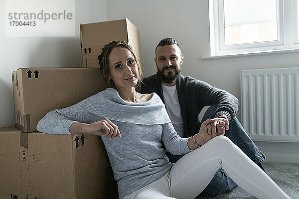 Junge Frau hält die Hand ihres Freundes  während sie sich in ihrer neuen Wohnung auf Kartons stützt