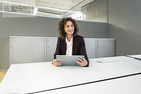 Geschäftsfrau mit digitalem Tablet  die wegschaut  während sie im Büro sitzt
