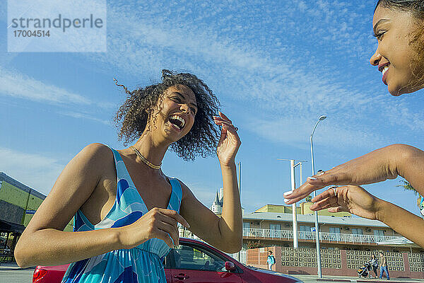 Junge Frau lacht  während sie eine Freundin in der Stadt an einem sonnigen Tag ansieht