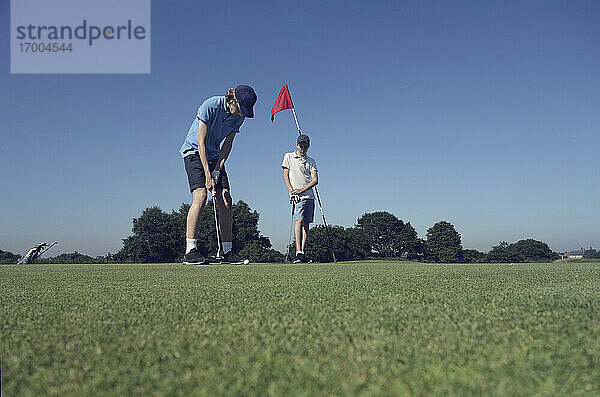 Freunde spielen Golf gegen den klaren blauen Himmel auf dem Platz