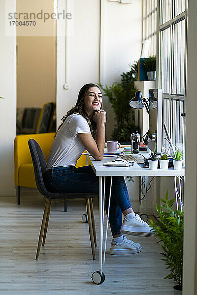 Junge Geschäftsfrau mit Hand am Kinn im Büro sitzend
