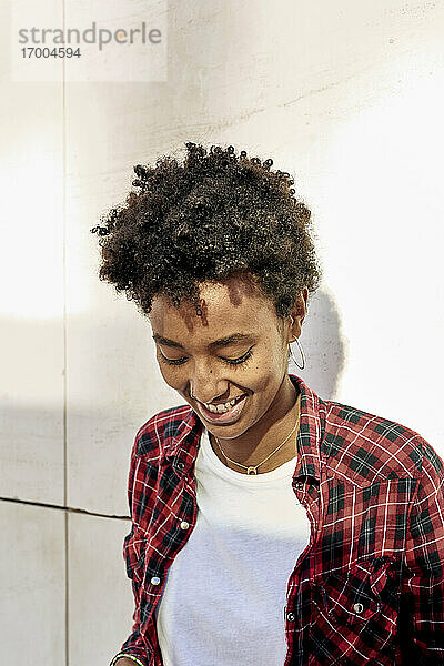Lächelnder junger weiblicher Afro-Hipster  der gegen eine weiße Wand blickt