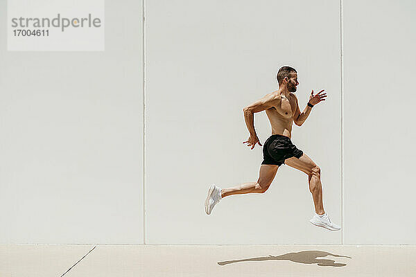 Männlicher Athlet mit nacktem Oberkörper  der gegen eine Wand springt