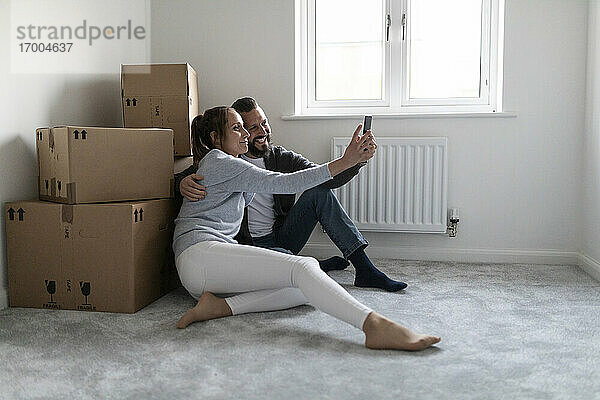 Lächelndes Paar macht Selfie mit Pappkartons zu Hause