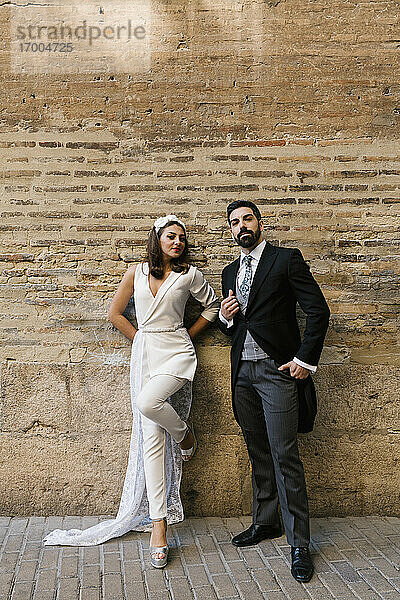Junges  frisch verheiratetes Paar  das auf dem Gehweg an der Wand steht