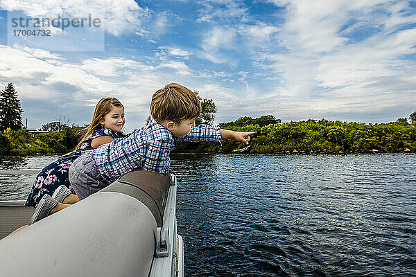 Junge  der mit seiner Schwester in einem Boot auf einem See gegen den Himmel zeigt