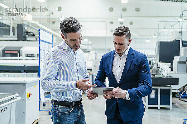 Geschäftsmann mit männlichem Kollegen bei der Arbeit an einem digitalen Tablet in einer Fabrik