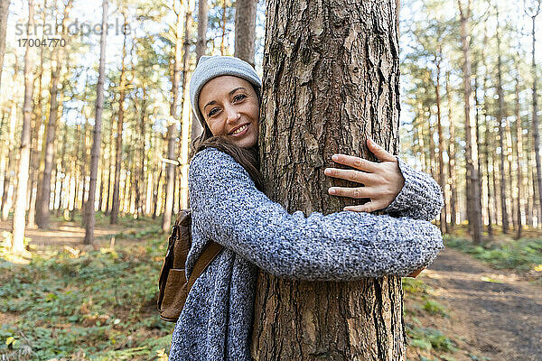 Lächelnde Wanderin  die einen Baumstamm umarmt  während sie im Cannock Chase Waldgebiet unterwegs ist