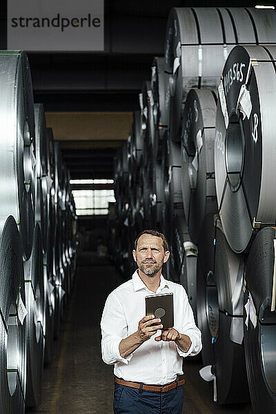 Nachdenklicher Geschäftsmann schaut weg  während er ein digitales Tablet in der Industrie hält