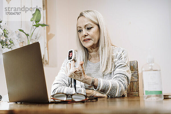Ältere Frau mit Pulsanzeige bei der Online-Beratung zu Hause