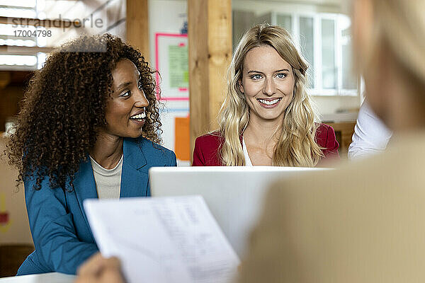 Lächelnde Geschäftsfrau mit Laptop bei der Arbeit mit Kollegen in einer Besprechung im Büro