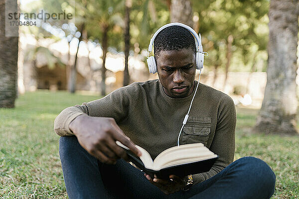 Männlicher Unternehmer liest ein Buch  während er im Park im Gras sitzt