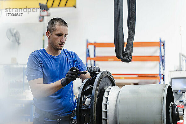 Männlicher Techniker  der eine Maschine repariert  während er in einer beleuchteten Fabrik steht